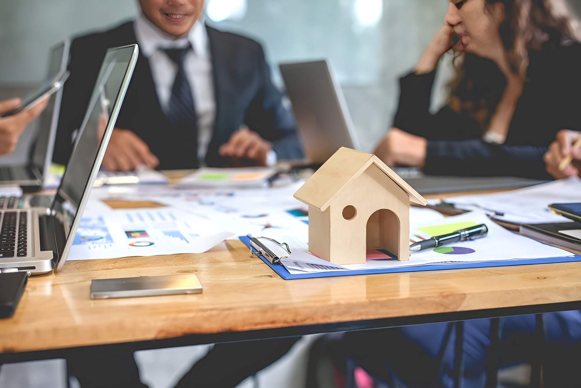 Accountant Are Sitting Around A Table With A Small Wooden House — Whitson Dawson Accountants in North Queensland