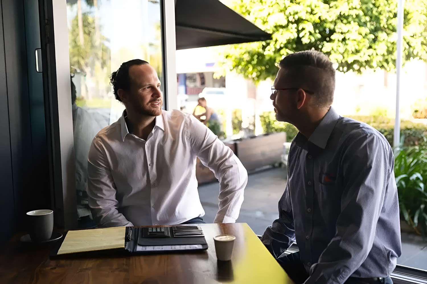 Two Men Are Seated At A Table Outdoors — Whitson Dawson Accountants in Central Queensland