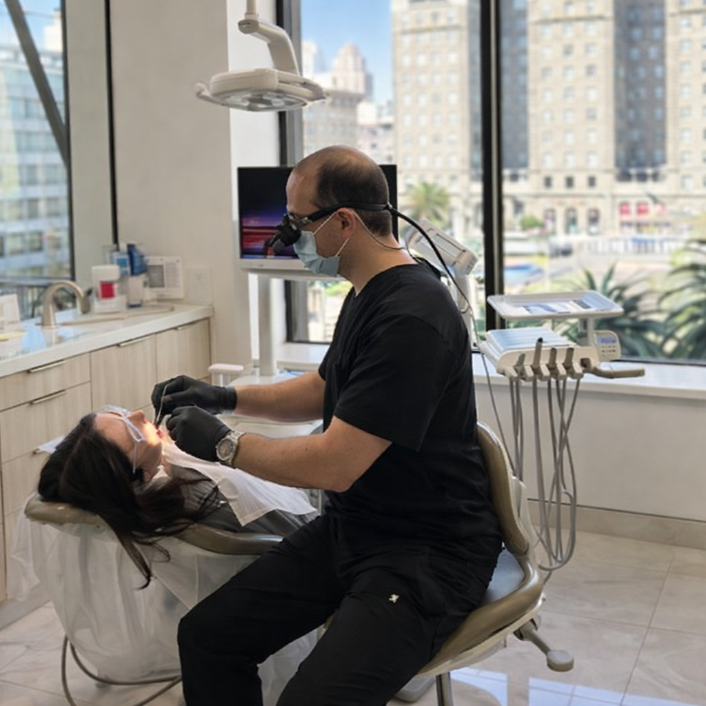 Dentist in black scrubs examining a patient in a chair at a bright clinic with city views.