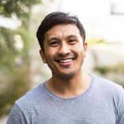 Smiling man in a gray T-shirt standing outdoors with a blurred background