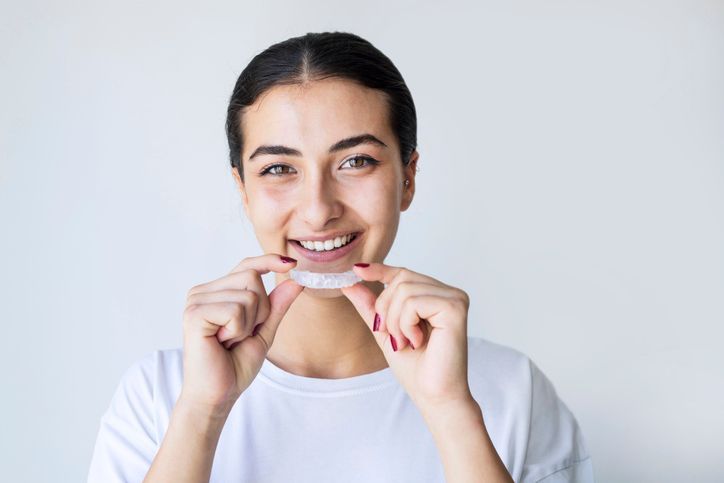 Woman smiling while holding clear dental aligners against a light background