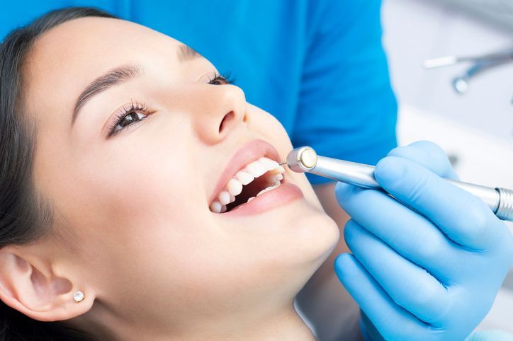 Dentist examining a patient’s mouth with a dental tool, wearing blue gloves and working in a clinic