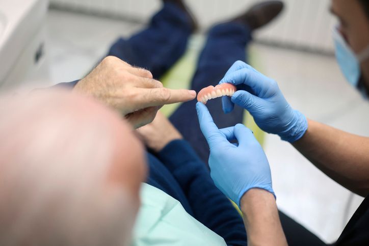 Gloved hands fitting a clear dental aligner onto a person’s teeth in a clinic