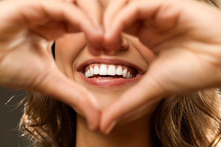 Smiling mouth framed by hands forming a heart shape