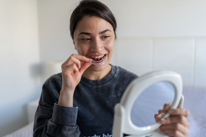 Woman flossing teeth while looking into a handheld mirror indoors