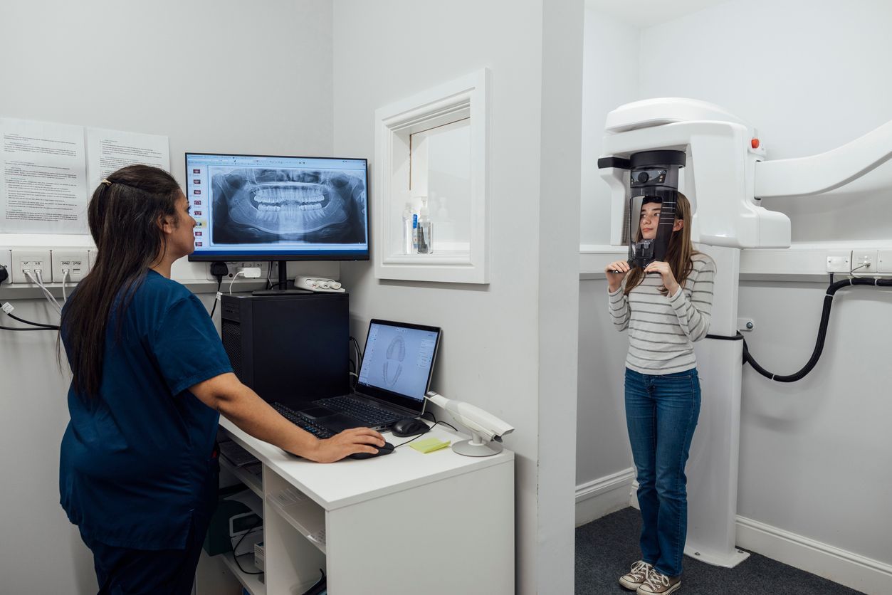 Dental office with a technician at a computer and a patient standing in an X-ray machine