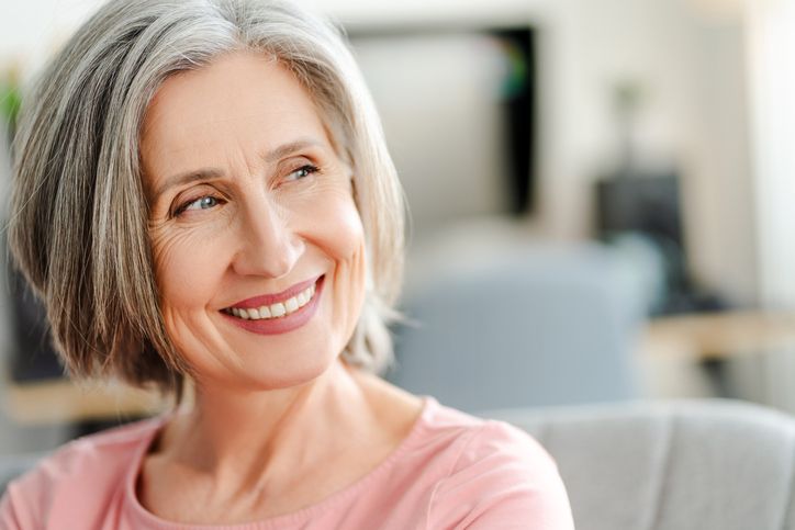Smiling gray-haired person in a pink shirt sitting on a couch