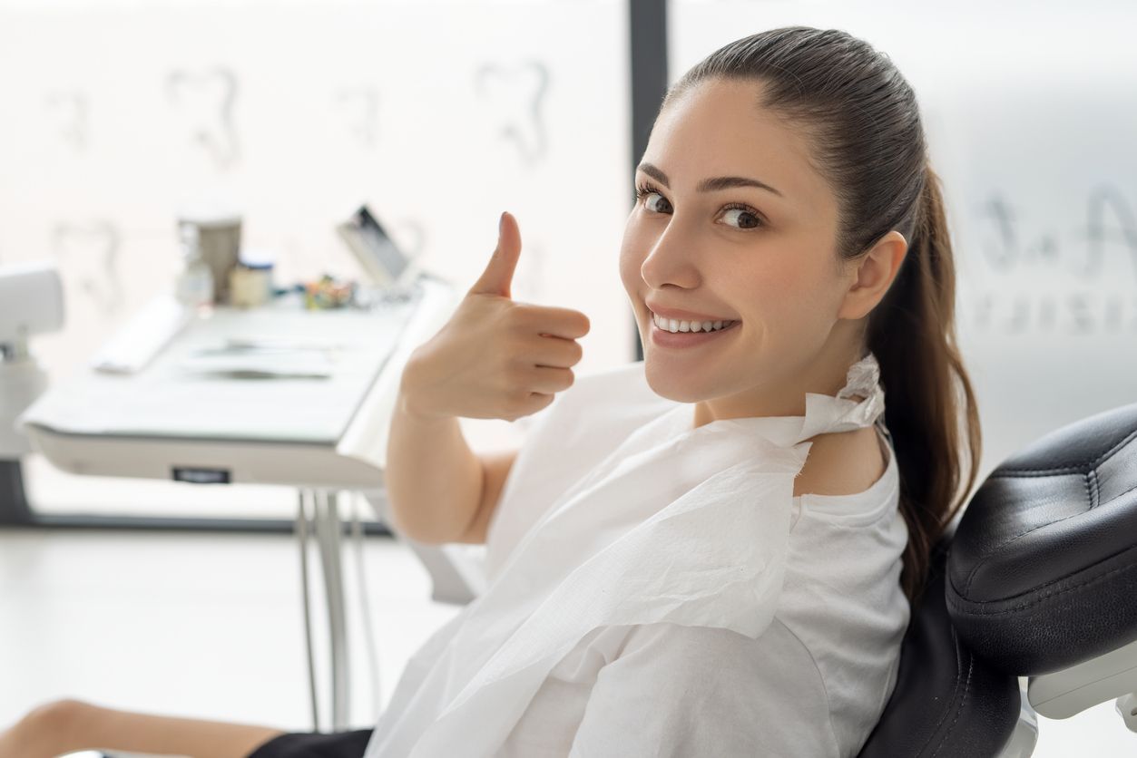 Smiling woman in a chair giving a thumbs-up in a bright office setting
