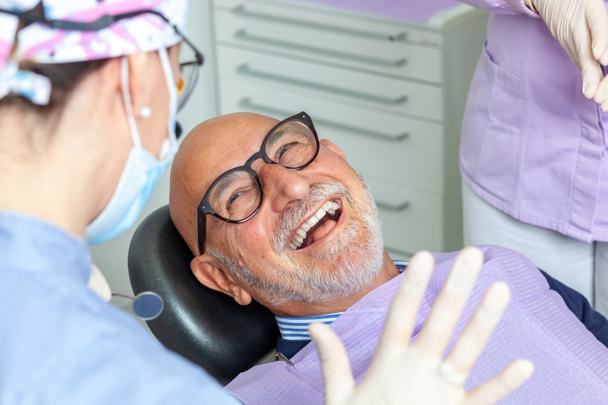 Smiling patient in dental chair during treatment, with dentist nearby and gloved hands in view