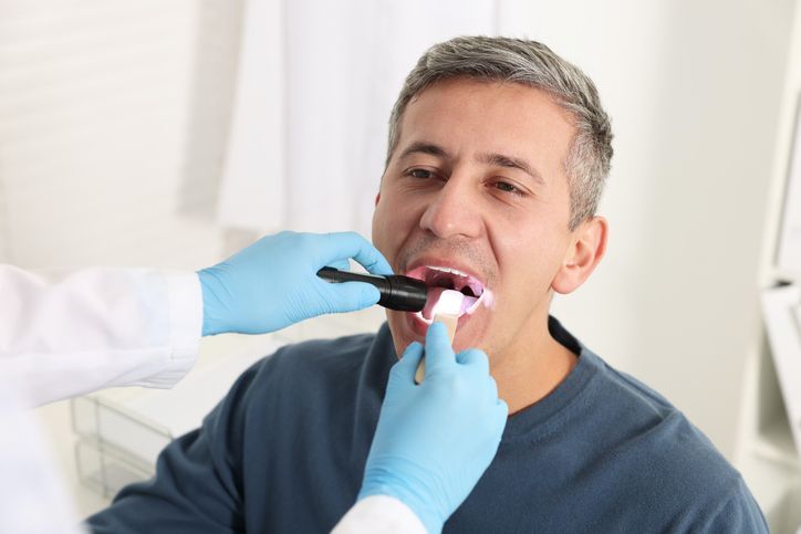 Dentist examining a patient’s mouth with gloved hands and a dental mirror in a bright clinic