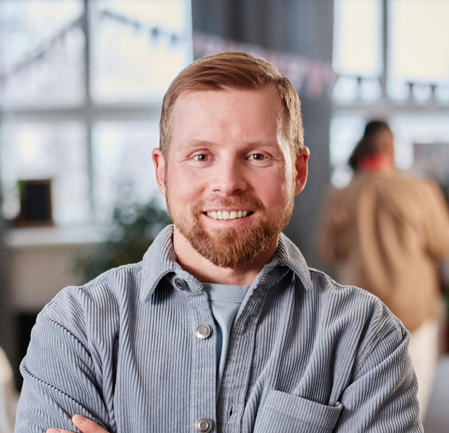 Smiling man in a gray T-shirt standing outdoors with a blurred background
