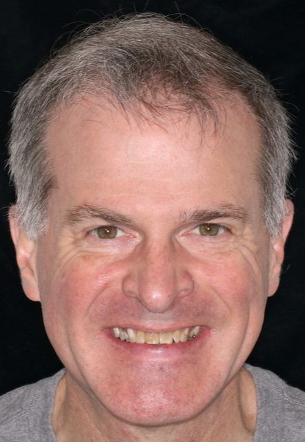 Smiling person with short gray hair against a dark background