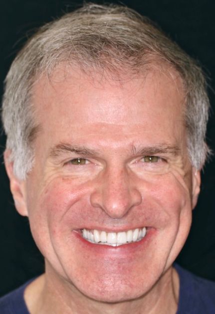 Smiling headshot of a man with short gray hair on a dark background