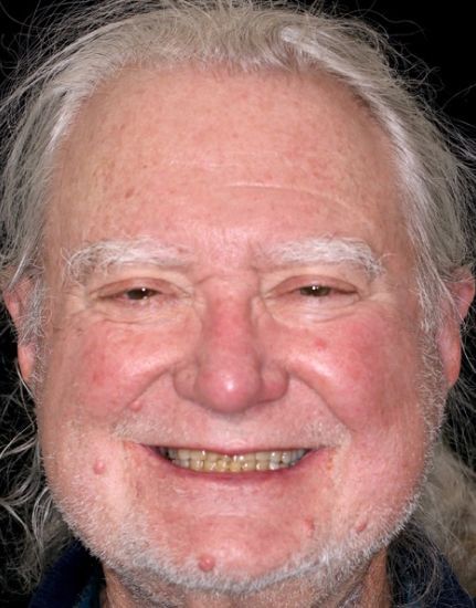 Close-up portrait of a smiling person with gray hair against a dark background