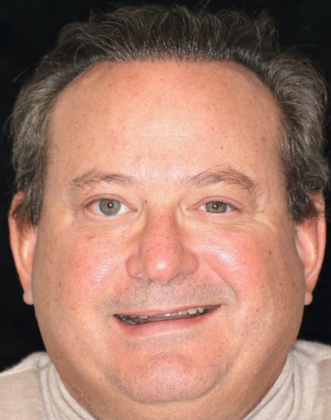 Close-up portrait of a smiling man against a dark background