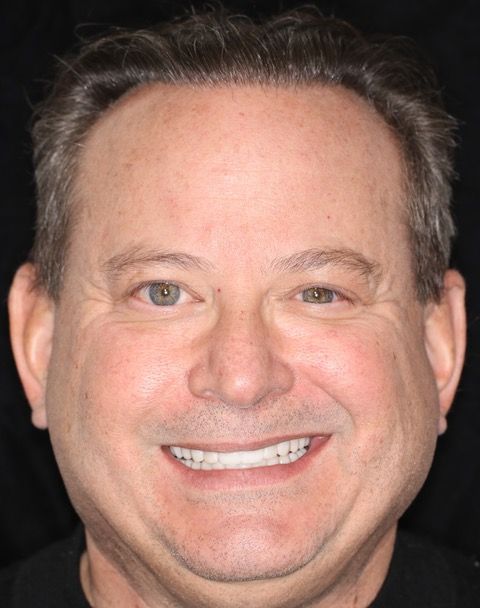 Close-up headshot of a smiling man against a dark background