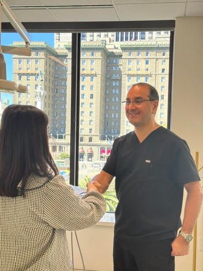 Two people shaking hands in an office with large windows and a city view.
