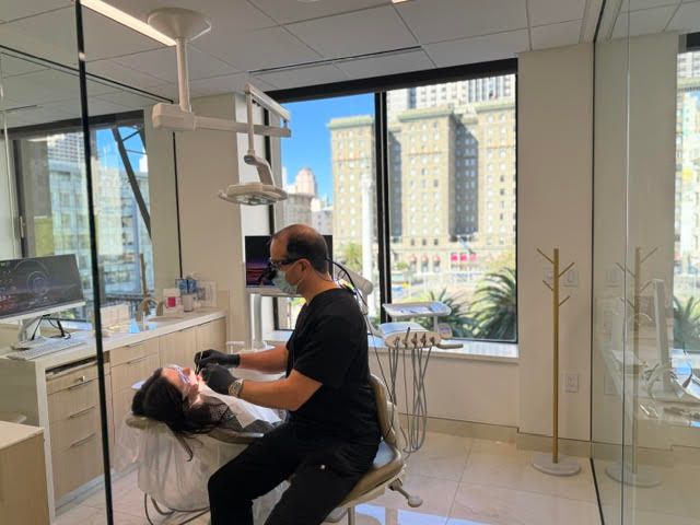 Dentist treating a patient in a bright clinic with large windows and city views