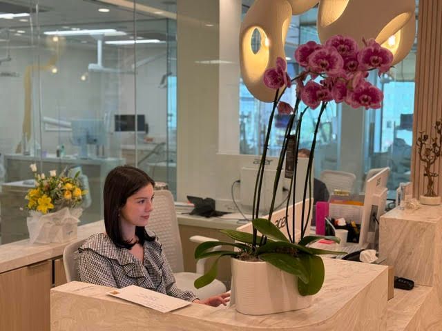 Woman working at a desk in a modern office, with a large pink orchid in the foreground.