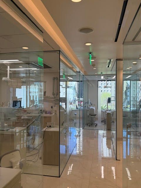 Glass-walled office hallway with desks, chairs, and reflections on a polished floor.