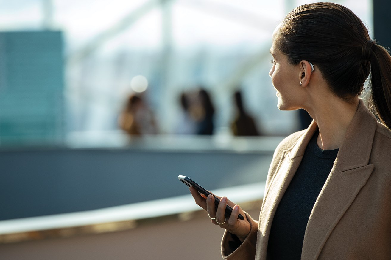 A woman wearing a hearing aid is holding a cell phone.
