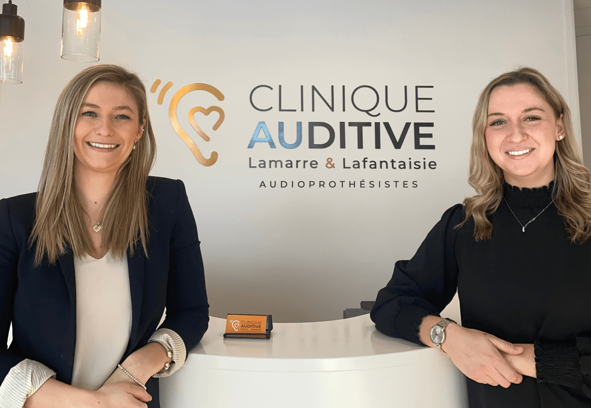 Deux femmes se tiennent l'une à côté de l'autre devant un panneau indiquant clinique auditive.