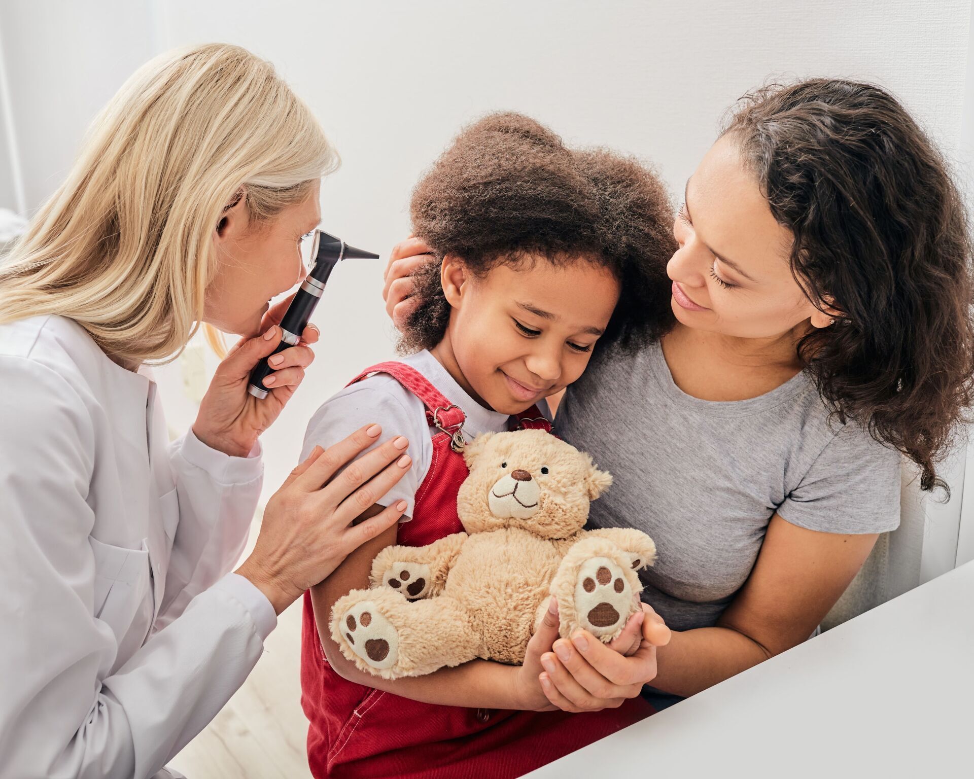 Une petite fille tient un ours en peluche pendant qu'un médecin examine son oreille.
