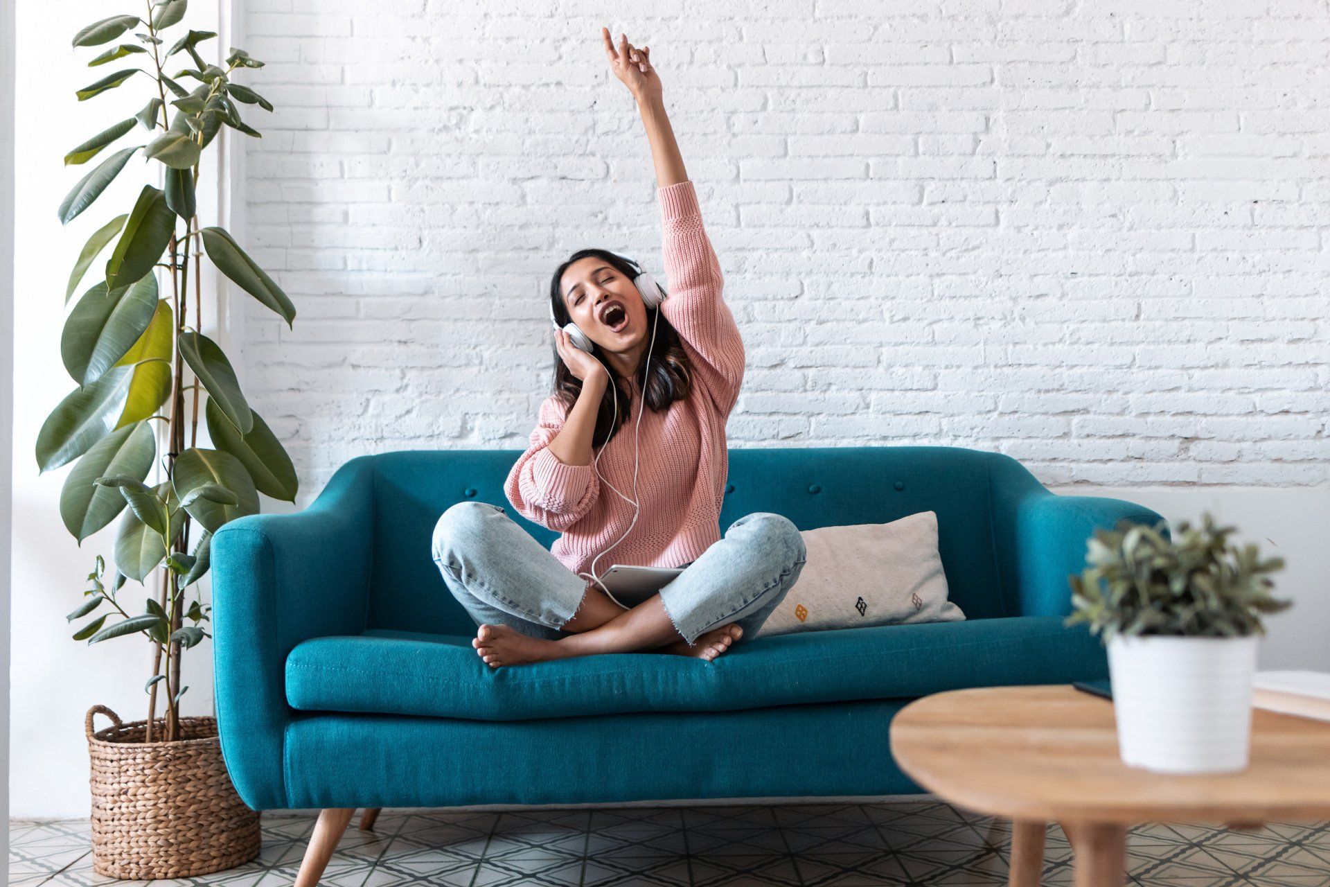 A woman is sitting on a blue couch wearing headphones and listening to music.