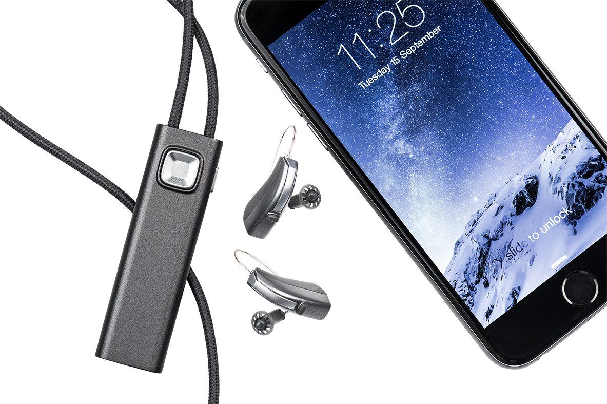 A cell phone with a pair of hearing aids attached to it.