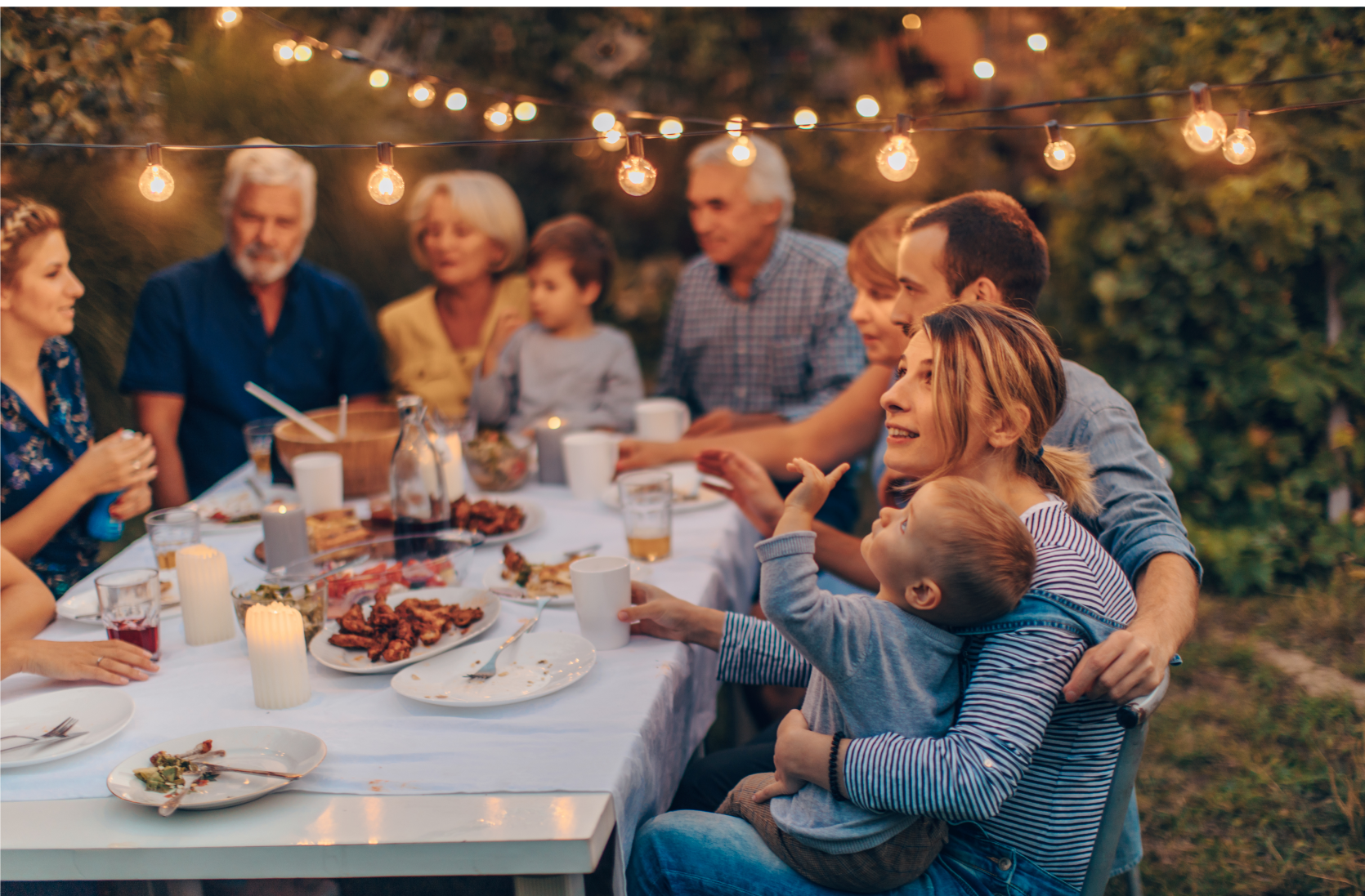 A large family is sitting around a table eating food.