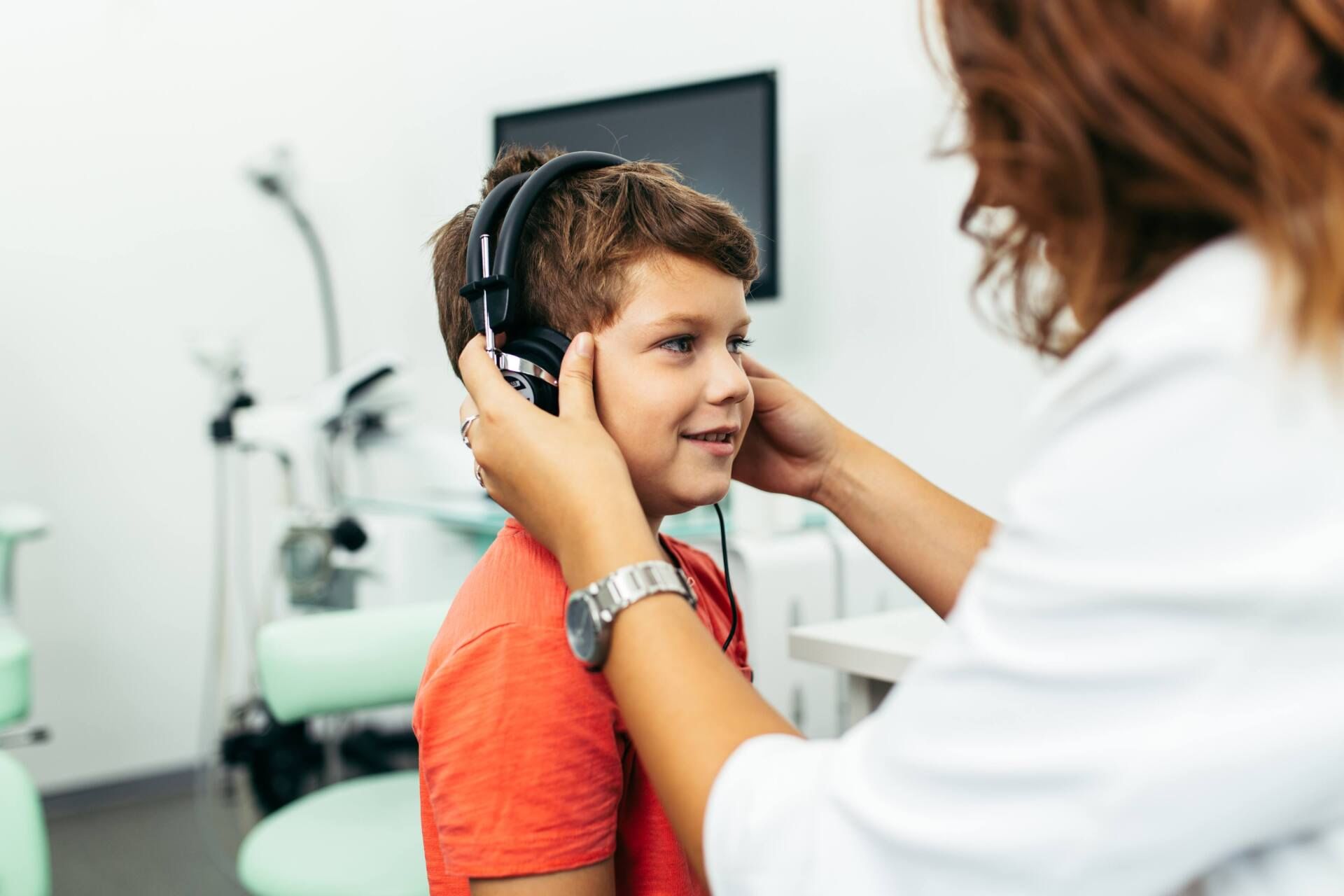 A doctor is putting headphones on a young boy 's ears.