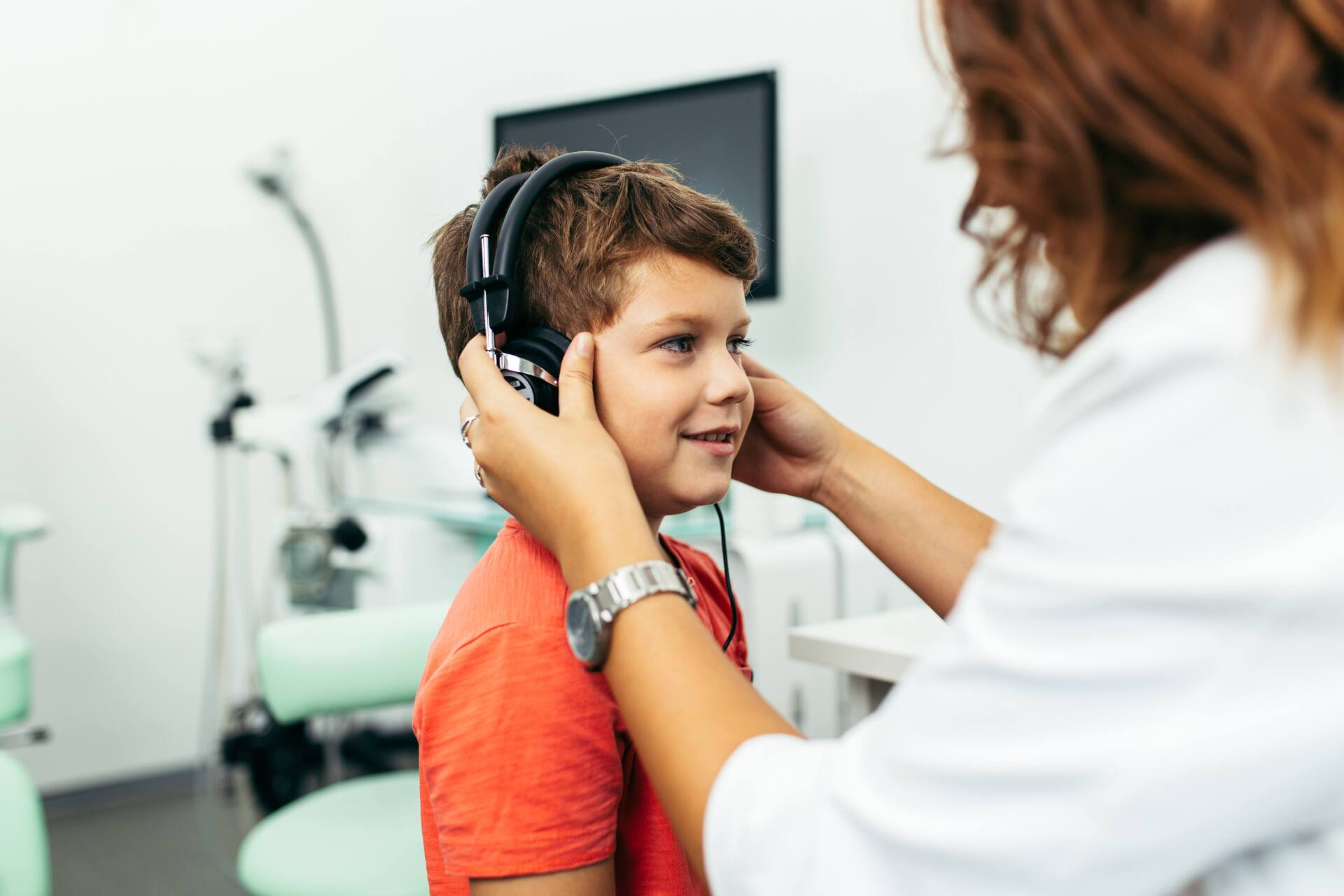 A doctor is putting headphones on a young boy 's ears.