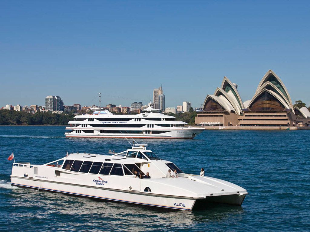 Two boats are floating in the water in front of the opera house.