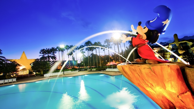 Mickey Mouse statue with water jets at a brightly lit theme park fountain at night