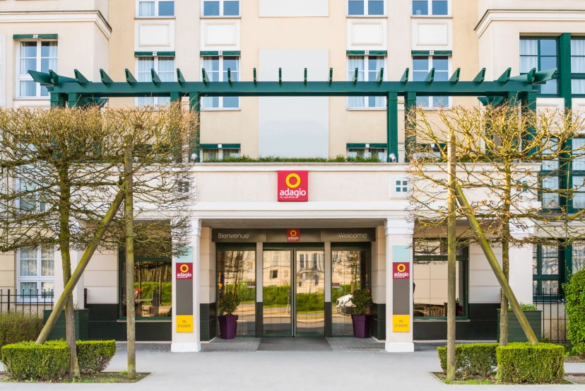 Apartment building entrance with glass doors, red sign, and trees along the walkway