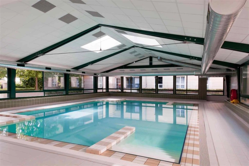 Indoor swimming pool with turquoise water, skylights, and large windows in a tiled room