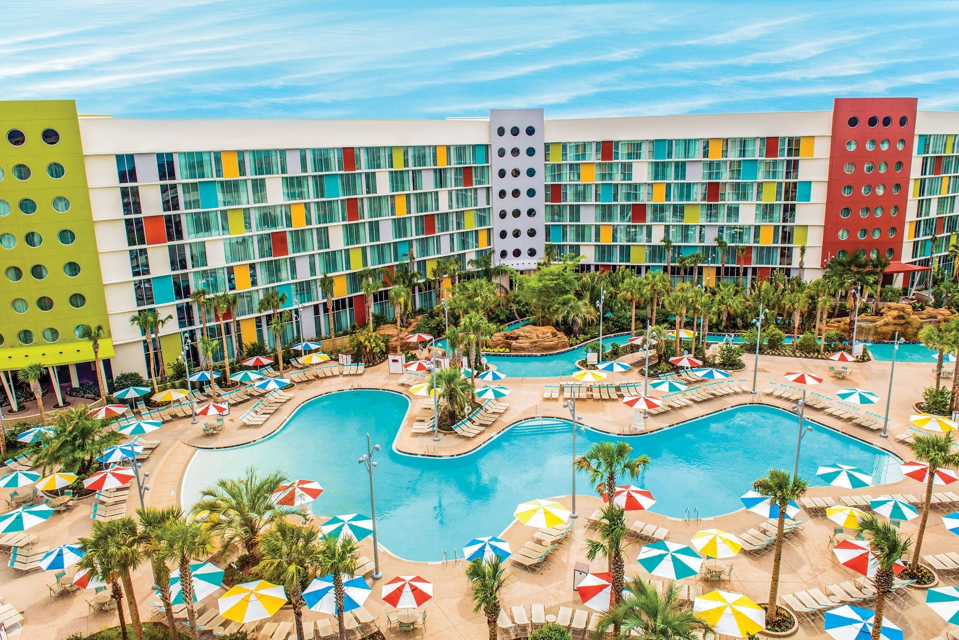 Colorful resort hotel with a large pool, palm trees, and lounge chairs by the ocean