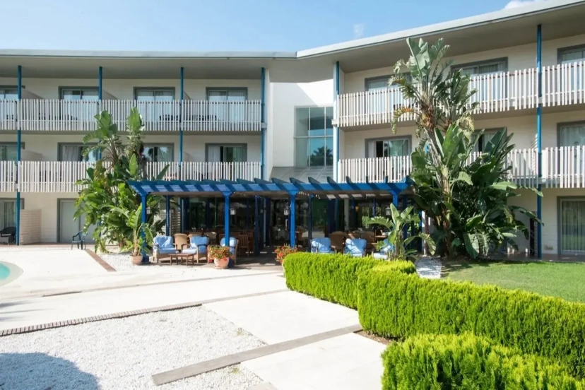 Modern apartment building with balconies, blue awning seating area, and trimmed hedges in front