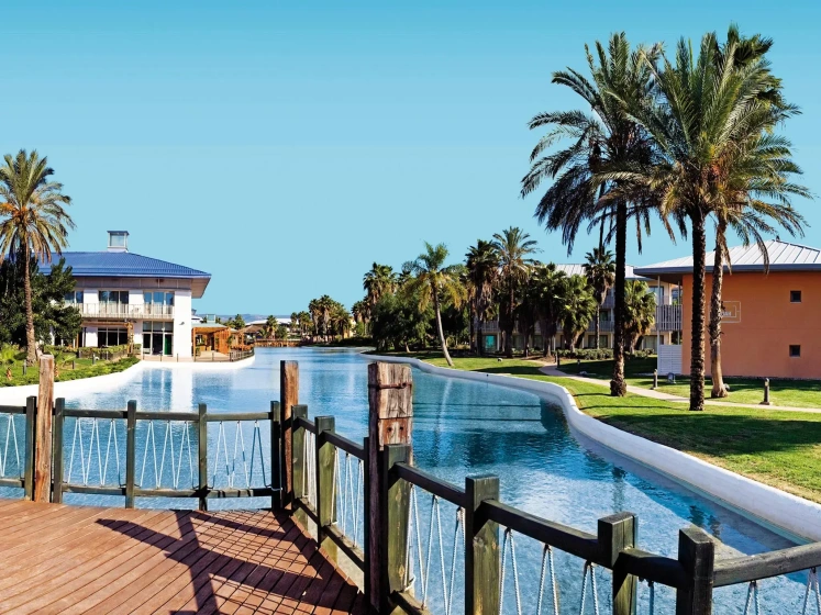 Resort canal with blue water, palm trees, and waterfront buildings under a clear sky
