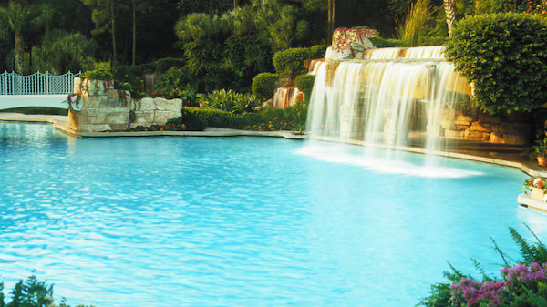 Blue resort pool with a small waterfall and lush greenery in the background