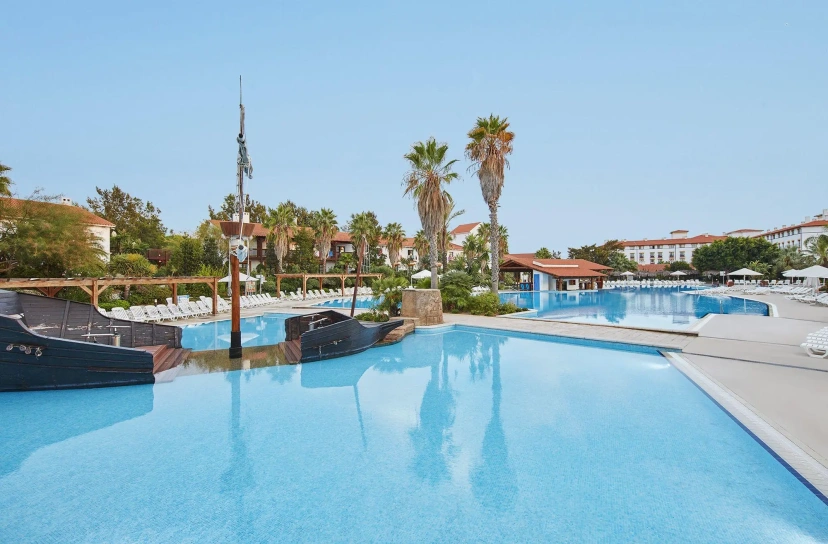 Resort pool with a blue infinity edge, palm trees, loungers, and clear sky in the background