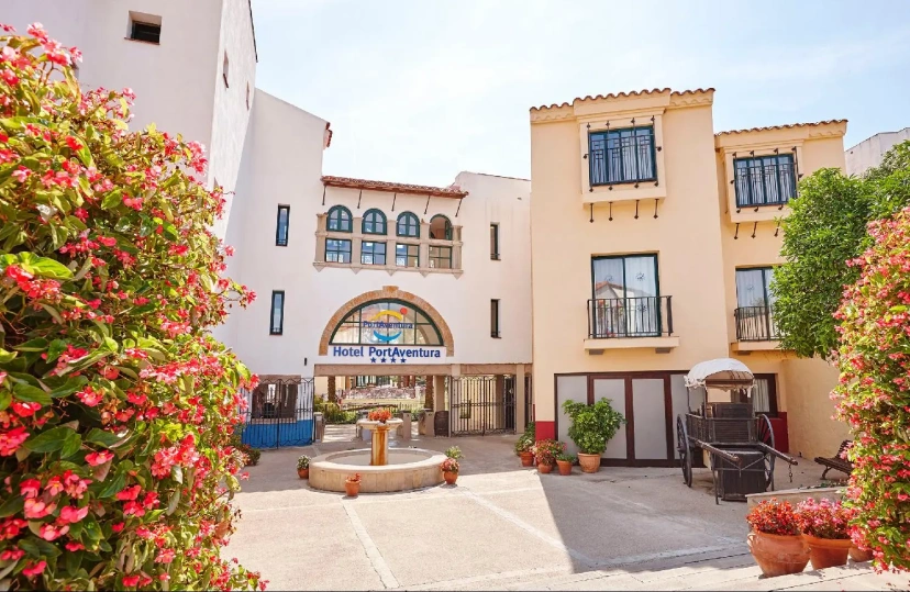 Sunlit courtyard entrance to a beige-and-blue building with flowers and potted plants
