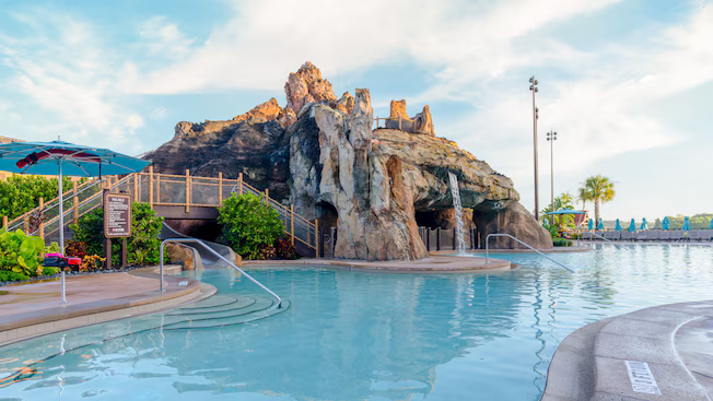 Rocky poolside grotto with a waterslide and palm-lined deck at a resort pool