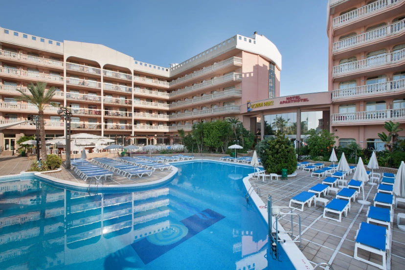 Hotel resort pool with blue lounge chairs and multi-story buildings on a sunny day
