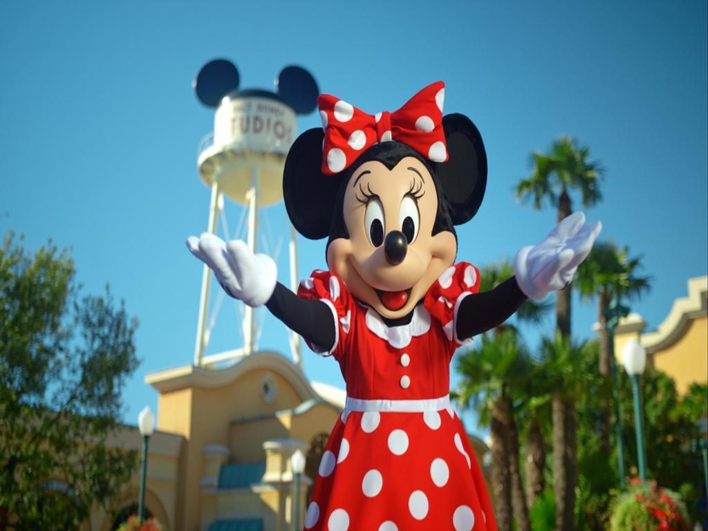 A minnie mouse mascot is standing in front of a water tower.