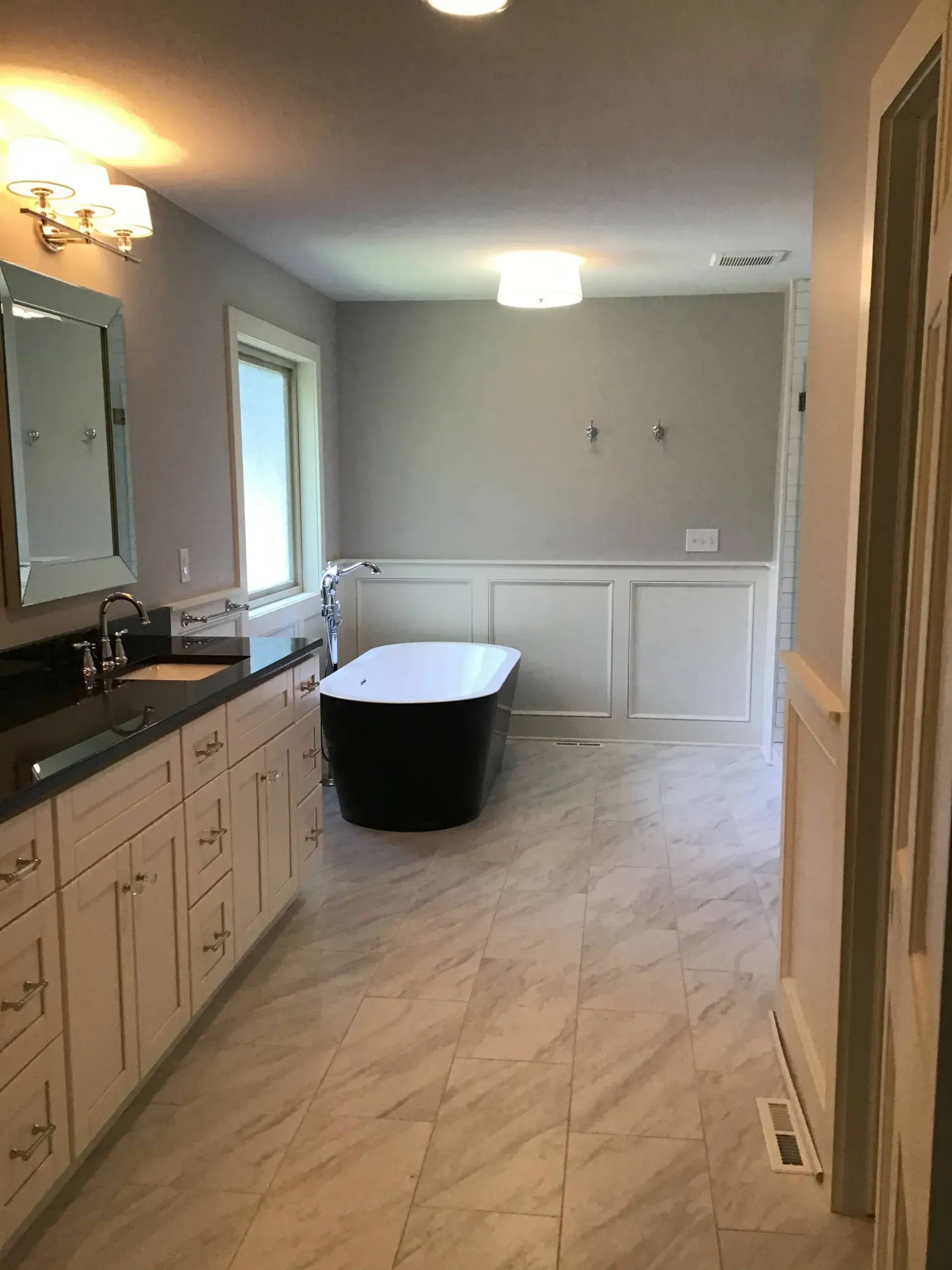 Empty bathroom with white tile floor, vanity, mirror, window, and a freestanding bathtub in a gray alcove.