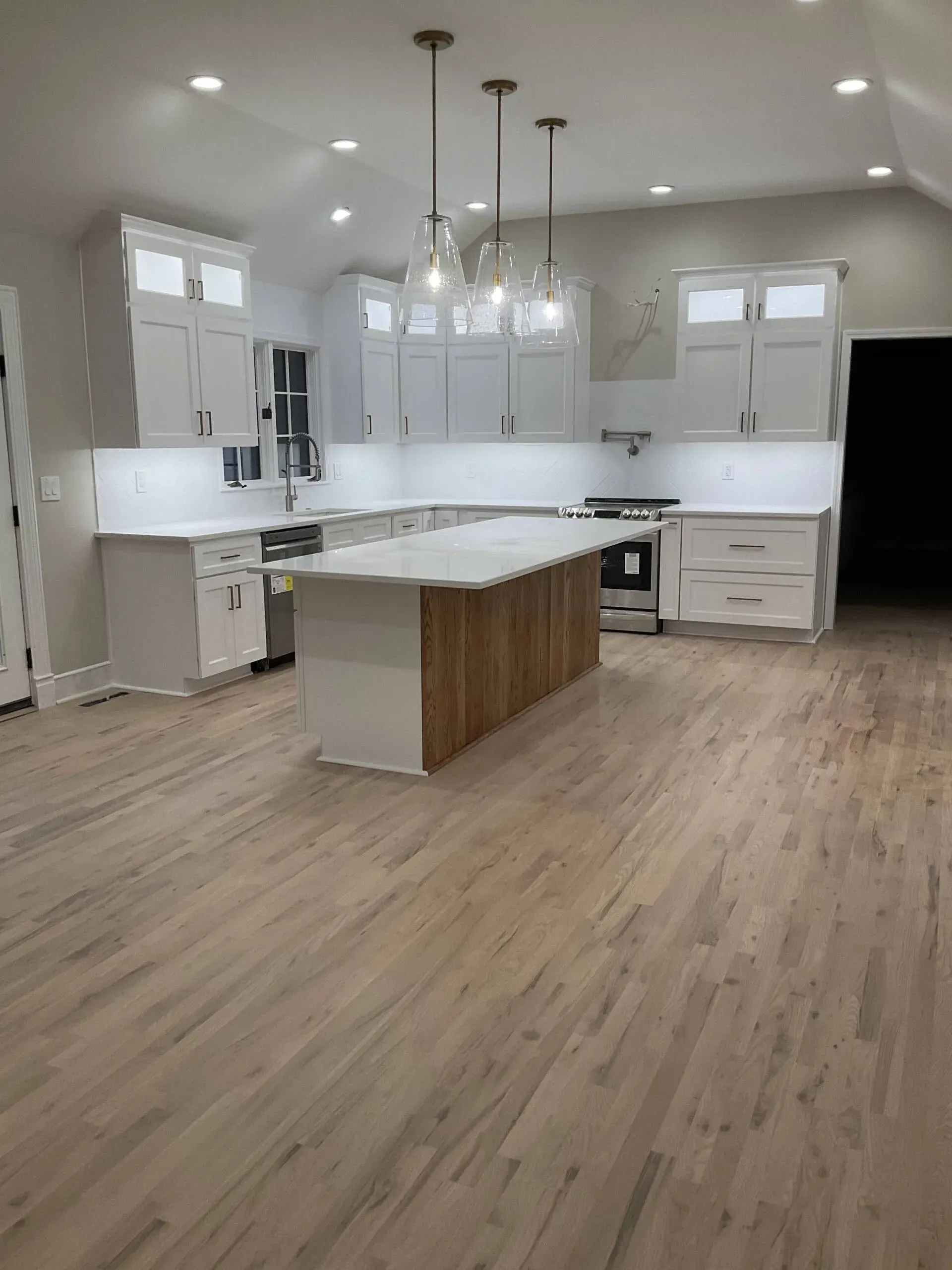Modern kitchen with light wood floor, white island, gray cabinets, and stainless steel appliances.
