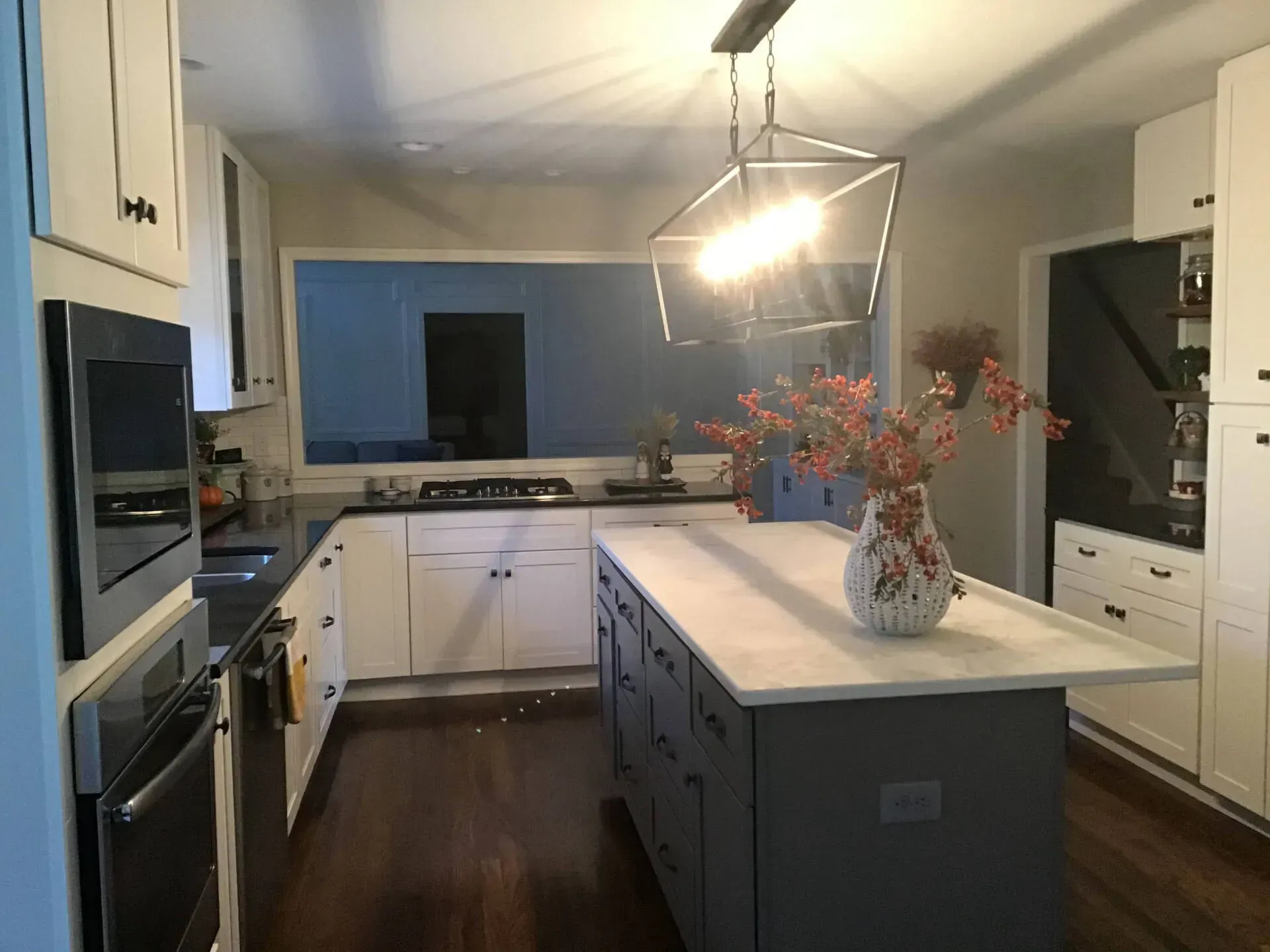 Modern kitchen with dark island, white cabinets, and a vase of flowers under pendant lights