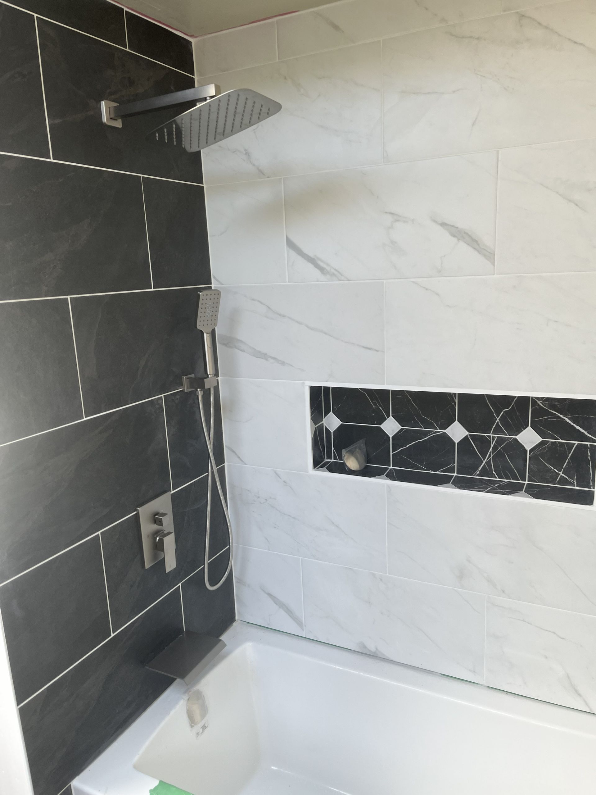 Modern bathroom shower with black and white tiled walls and a small shelf.