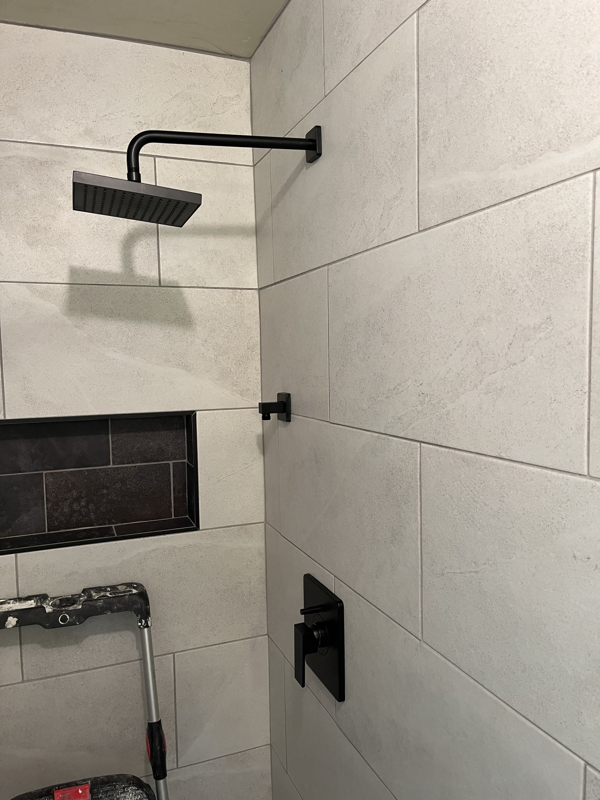 Tiled shower with black showerhead, handle, and fixtures beside a built-in shelf.